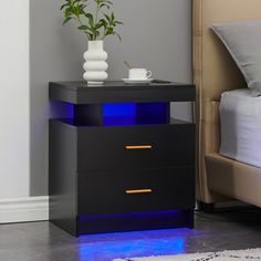 a night stand with two drawers and a blue light on the bottom, next to a bed