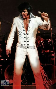 elvis presley performing on stage with microphone in his hand and other musical instruments behind him