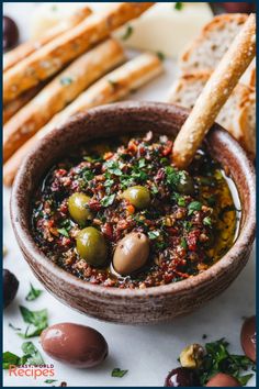 a bowl filled with olives and bread on top of a white table next to other food