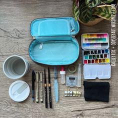 an artist's kit with watercolors, brushes and other supplies on a wooden table