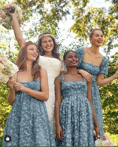 four bridesmaids in blue dresses holding bouquets and smiling at the camera with their arms around each other