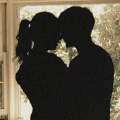 two people standing in front of a window with their arms around each other's shoulders