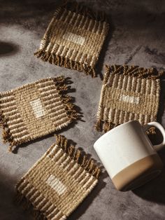 Set of four handwoven coasters with earthy tones, arranged on a rustic surface alongside a ceramic mug. Weaving Coasters Diy, African Weaving, Woven Coasters, Wool Coasters, Weaving Loom Diy, Entertaining Gifts, Diy Coasters, Weaving Projects, Little Designs