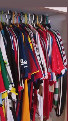 a rack full of different colored shirts hanging on the side of a wall next to a door