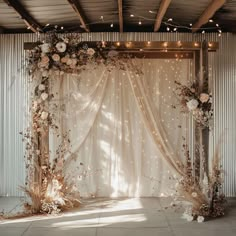 a white backdrop with flowers and lights on the wall is decorated with sheer curtains for an outdoor wedding ceremony