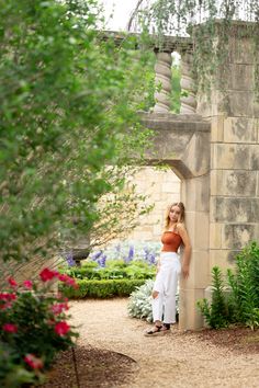 a woman leaning against a stone wall in a garden