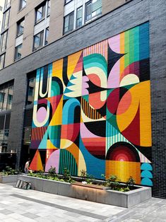 a large colorful mural painted on the side of a building next to a planter