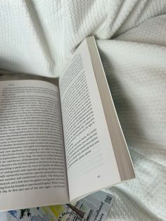 an open book sitting on top of a bed next to a white comforter and pillows