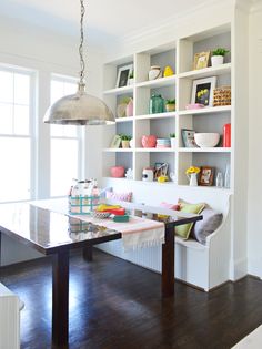 a dining room with white walls and wooden flooring, built in shelving units