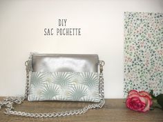 a silver purse sitting on top of a wooden table next to a pink flower and wall