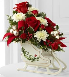 a white sleigh with red and white flowers in it sitting on a table