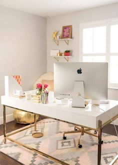 a desk with a computer on top of it in front of a window and a rug