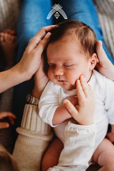 a woman holding a baby in her arms and touching it's ear with both hands