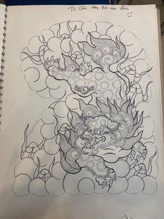 a drawing of a dragon with clouds and water in the background, on top of a notebook