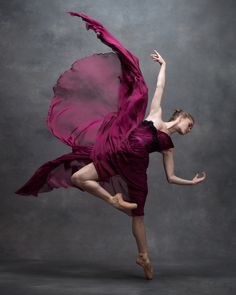 a woman in a purple dress is dancing with her arms spread out and legs extended