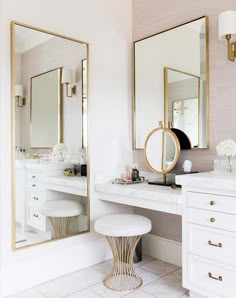 a white and gold bathroom with two mirrors on the wall, stools in front of it