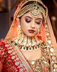 a woman in a red and gold bridal outfit with jewels on her head, wearing a