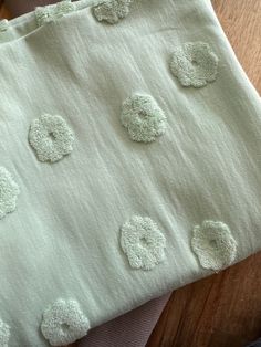 a close up of a piece of cloth on a wooden table with white fabric and green flowers