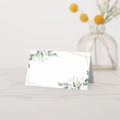 a white card with green leaves on it next to a vase filled with oranges