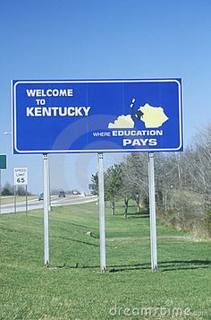 a welcome to kentucky sign in front of a highway with trees and grass on both sides