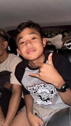 a young boy sitting in the back seat of a car giving a thumbs up sign