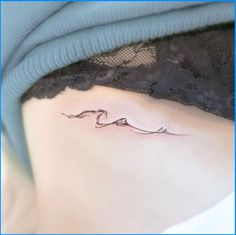 a woman's stomach with a small wave tattoo on her side ribcage