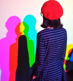 a woman standing in front of a rainbow colored wall with her shadow cast on the wall