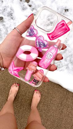 a person is holding a pink case with various items in it and her feet are on the sand