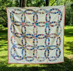 a quilt hanging on a clothes line in the grass with trees and grass behind it