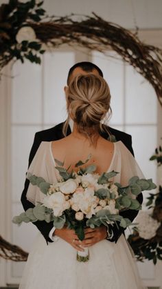 a bride and groom standing in front of a wreath