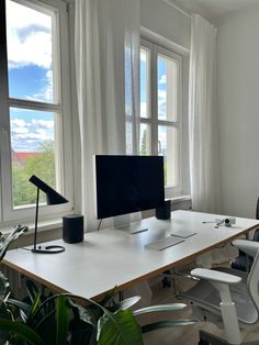 a desk with a computer monitor, keyboard and mouse on it in front of two windows