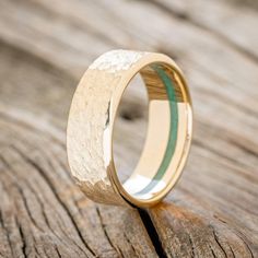 a gold wedding ring with a green stripe in the center on top of a wooden surface