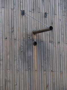 a clock on the side of a wooden building with pipes attached to it's sides