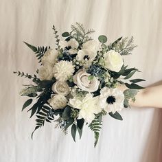 a bouquet of white flowers and greenery is held by a woman's hand