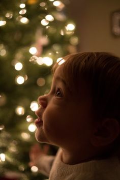 a young child standing in front of a christmas tree looking up at the ceiling with lights on it