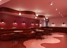 an empty restaurant with round tables and leather seating, red walls and lights on the ceiling