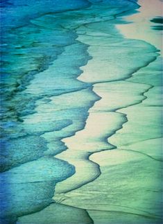 the water is blue and green with waves coming in from the ocean shore, as seen from above