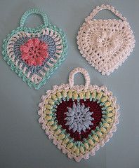 three crocheted heart shaped bags hanging on a gray wall next to each other