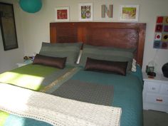 a bed with green and brown sheets in a bedroom next to a dresser, lamp and pictures on the wall