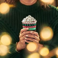 a woman holding a cup of coffee with whipped cream and candy canes on it