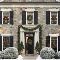 the front entrance to a large stone house decorated with christmas wreaths and potted plants