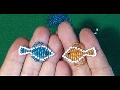 two small beaded fish sitting on top of someone's hand next to each other