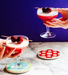 two people are holding glasses with drinks in them and one has cherries on the rim