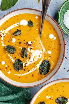 two bowls filled with carrot soup and topped with spinach garnished with cream