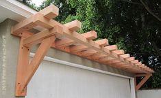 a wooden pergolan attached to the side of a building with trees in the background