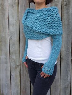 a woman standing in front of a wooden fence wearing a blue knitted shawl