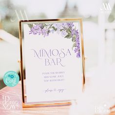 a close up of a sign on a table with purple flowers and leaves in the background