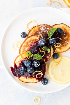 pancakes with blueberries and lemon slices on a white plate