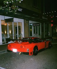 a red sports car is parked in front of a building at night with its hood up