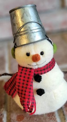 a small snowman with a tin hat and scarf on it's head sitting on a tile floor